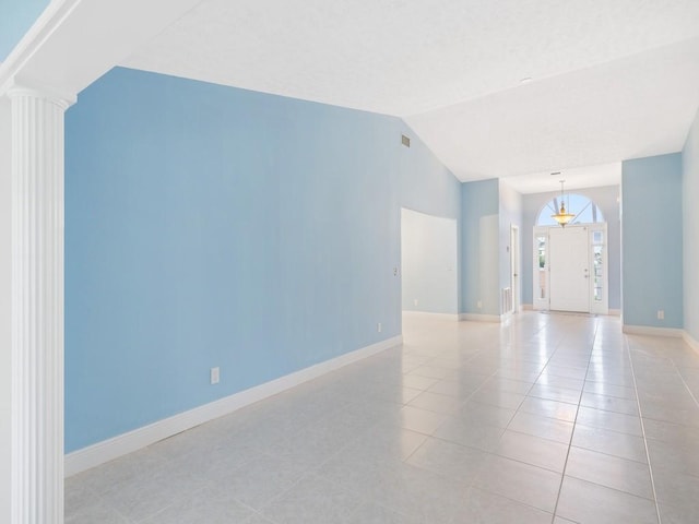 empty room with light tile patterned floors, ornate columns, visible vents, vaulted ceiling, and baseboards