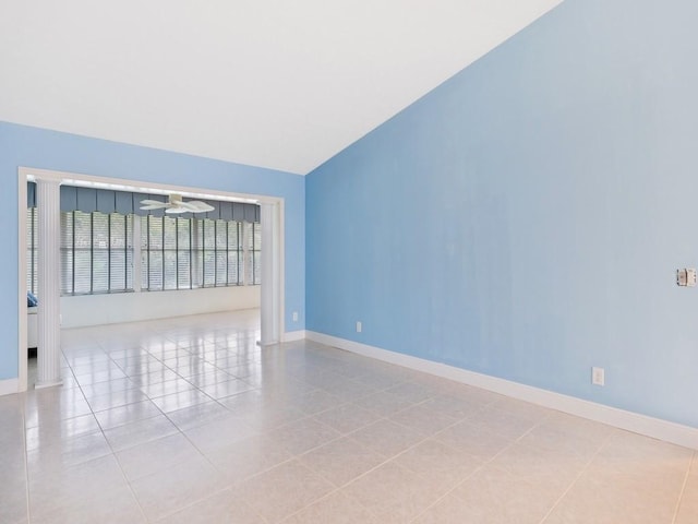 spare room with lofted ceiling, light tile patterned flooring, a ceiling fan, and baseboards