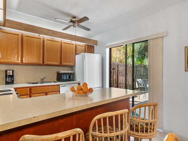 kitchen featuring a textured ceiling, sink, a kitchen breakfast bar, white appliances, and ceiling fan