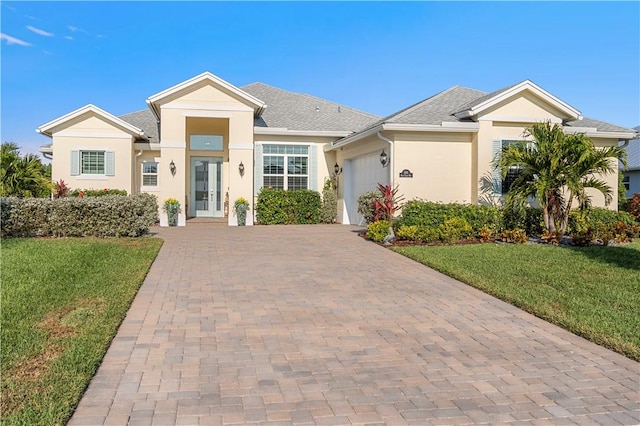 ranch-style house featuring an attached garage, a front yard, decorative driveway, and stucco siding