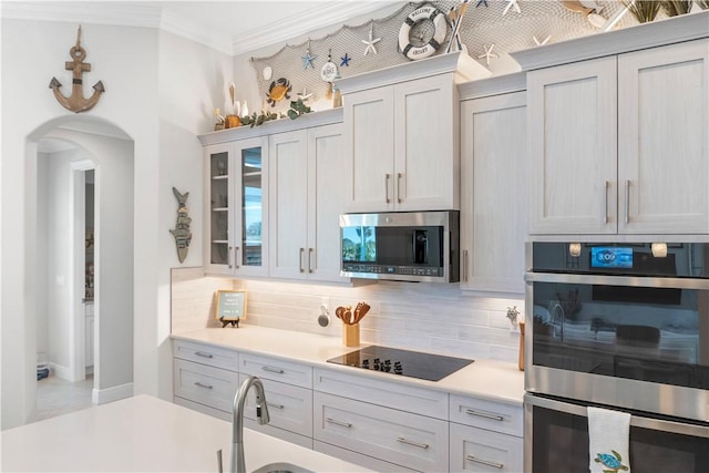 kitchen featuring arched walkways, light countertops, appliances with stainless steel finishes, tasteful backsplash, and crown molding