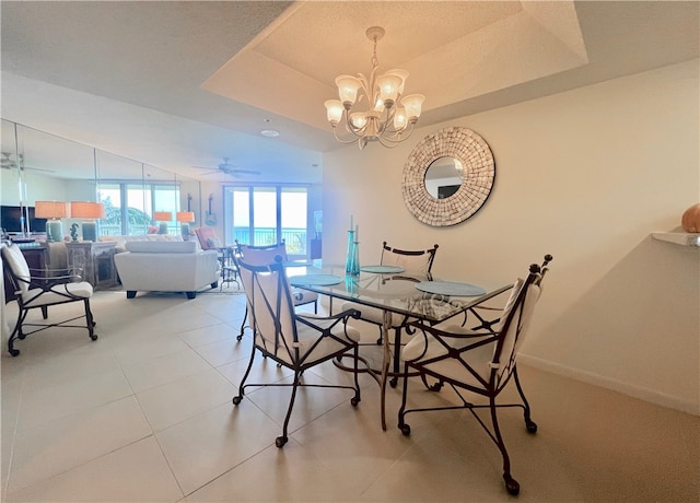 dining space featuring ceiling fan with notable chandelier, light tile patterned floors, and a tray ceiling