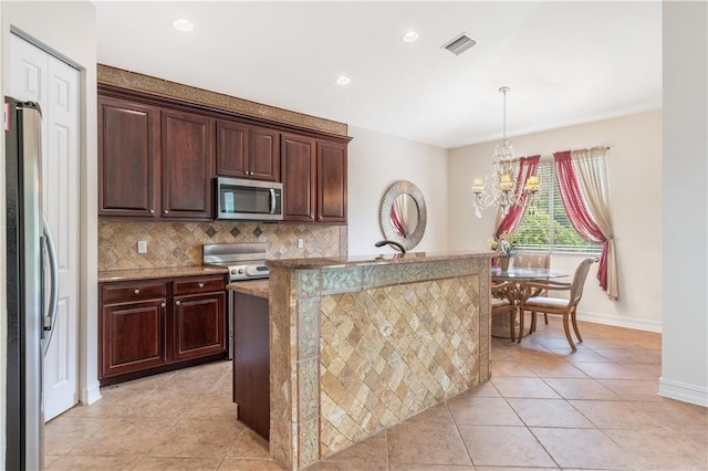 kitchen featuring tasteful backsplash, a center island with sink, visible vents, appliances with stainless steel finishes, and decorative light fixtures