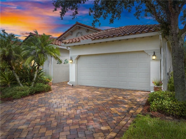 exterior space with a garage, decorative driveway, a tile roof, and stucco siding