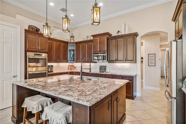 kitchen with light stone countertops, sink, pendant lighting, a center island with sink, and appliances with stainless steel finishes