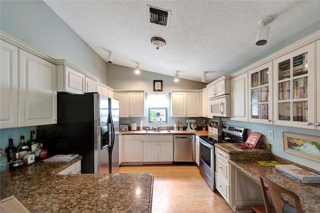 kitchen featuring lofted ceiling, sink, light hardwood / wood-style flooring, stainless steel appliances, and dark stone counters