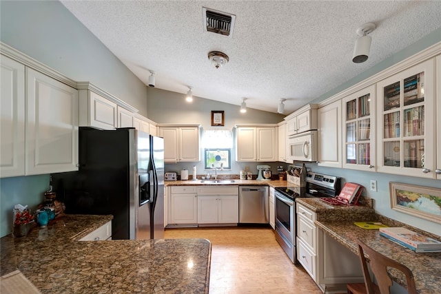 kitchen featuring sink, appliances with stainless steel finishes, dark stone countertops, white cabinetry, and vaulted ceiling