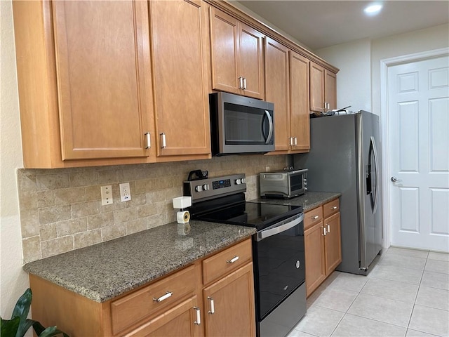 kitchen with brown cabinets, dark stone countertops, backsplash, appliances with stainless steel finishes, and light tile patterned floors