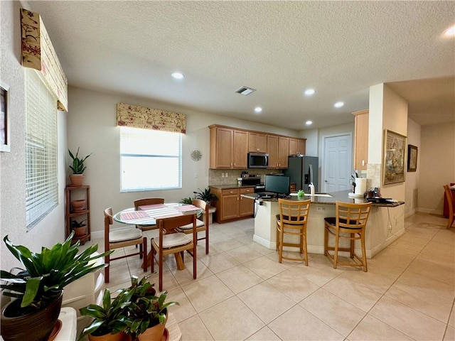 kitchen featuring light tile patterned floors, visible vents, a peninsula, appliances with stainless steel finishes, and a kitchen bar