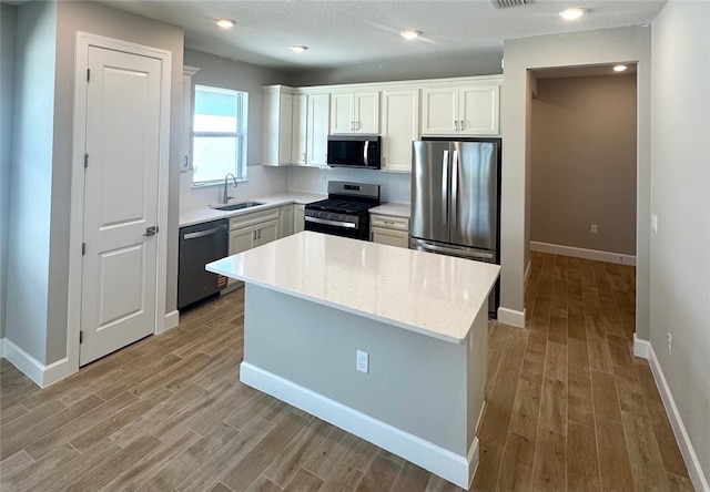kitchen with appliances with stainless steel finishes, a sink, wood finished floors, white cabinets, and recessed lighting