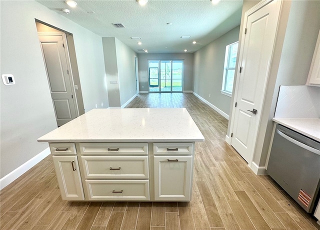 kitchen with stainless steel dishwasher, light wood finished floors, baseboards, white cabinets, and a textured ceiling