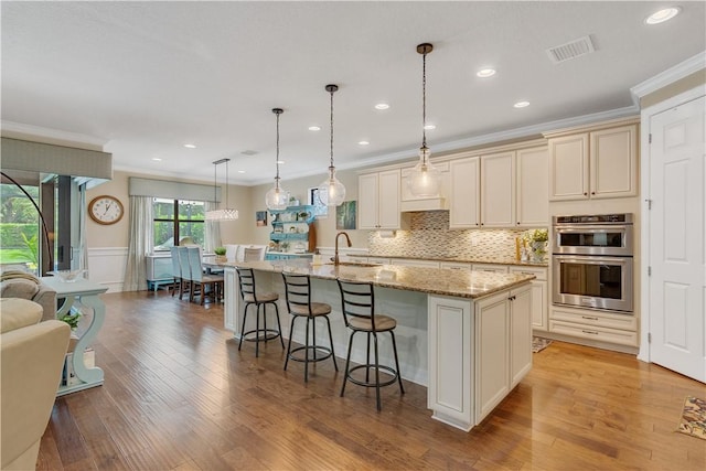 5417 Antigua Cir, Vero Beach, FL 32967 - kitchen featuring ornamental molding, a breakfast bar, double oven, cream cabinetry, and light wood finished floors