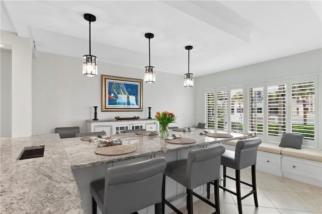 kitchen with a kitchen breakfast bar, light stone counters, white cabinets, and light tile patterned flooring