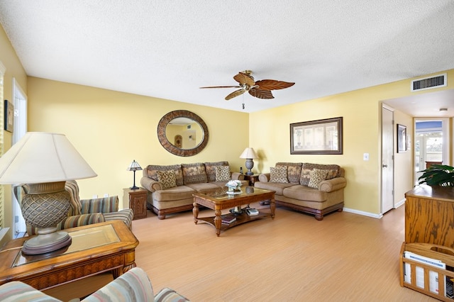 living room with light hardwood / wood-style floors, ceiling fan, and a textured ceiling