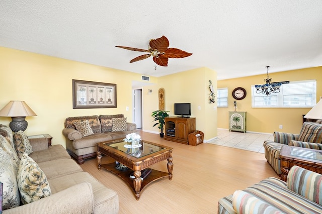 living room featuring ceiling fan with notable chandelier, a textured ceiling, and light hardwood / wood-style flooring