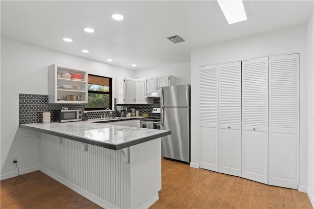 kitchen featuring stainless steel appliances, light wood finished floors, a peninsula, and visible vents