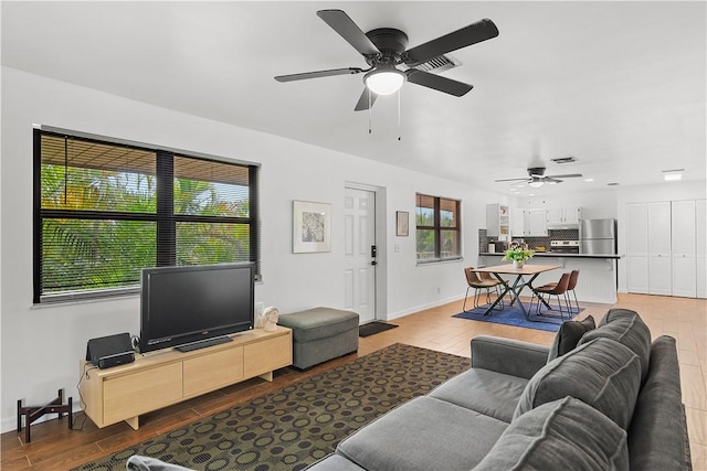 living room with visible vents, ceiling fan, light wood-style flooring, and baseboards