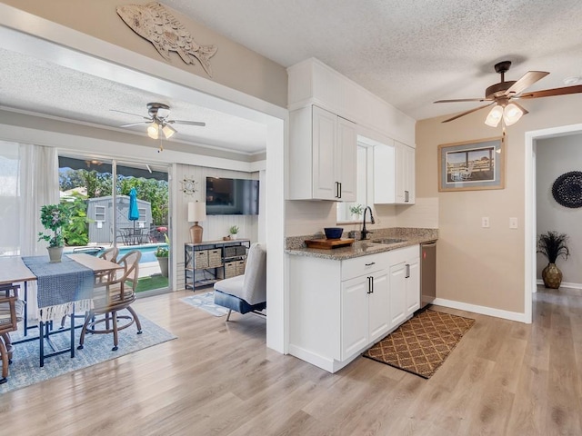 kitchen featuring ceiling fan, light wood-type flooring, a textured ceiling, white cabinets, and a sink