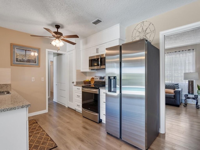 kitchen with appliances with stainless steel finishes, white cabinets, a textured ceiling, and visible vents