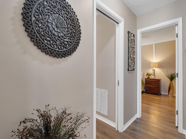 hall featuring baseboards, a textured ceiling, wood finished floors, and visible vents