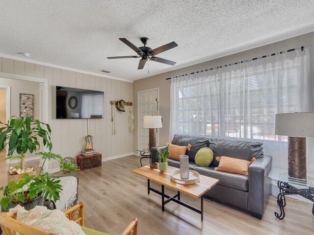 living room featuring ceiling fan, a textured ceiling, baseboards, wood finished floors, and ornamental molding