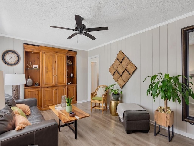 living room with crown molding, a ceiling fan, a textured ceiling, and light wood-type flooring