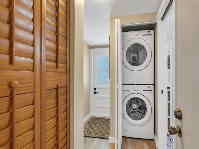 washroom featuring stacked washer and dryer, baseboards, laundry area, and light wood-style floors