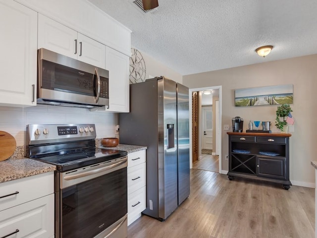 kitchen with white cabinets, appliances with stainless steel finishes, a textured ceiling, light wood-style flooring, and backsplash