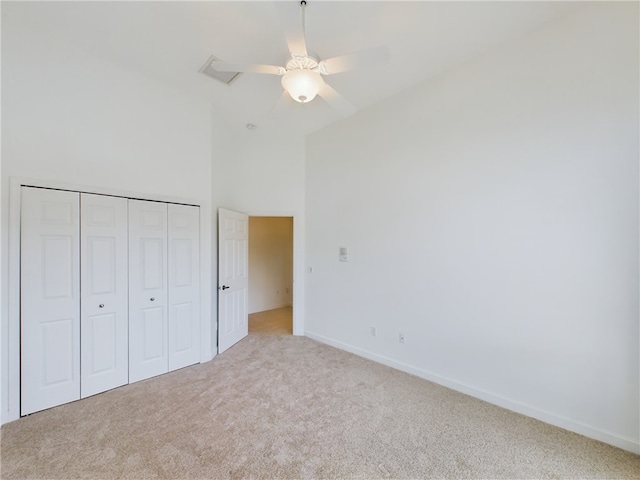 unfurnished bedroom with a closet, light colored carpet, a high ceiling, ceiling fan, and baseboards