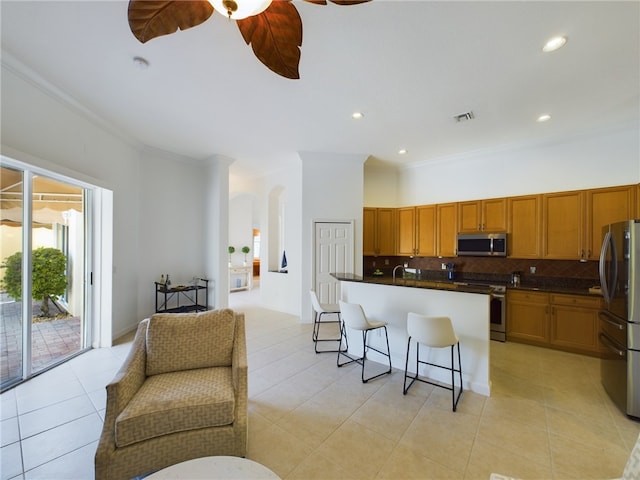 kitchen featuring tasteful backsplash, dark countertops, appliances with stainless steel finishes, open floor plan, and a kitchen bar