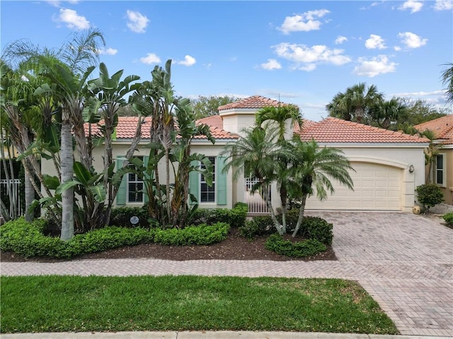 mediterranean / spanish-style home with a garage, decorative driveway, a tile roof, and stucco siding