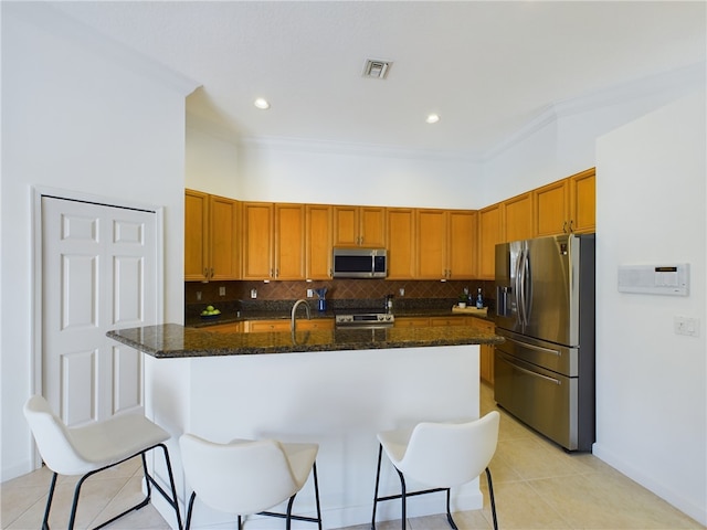 kitchen featuring dark stone counters, appliances with stainless steel finishes, an island with sink, and a kitchen bar