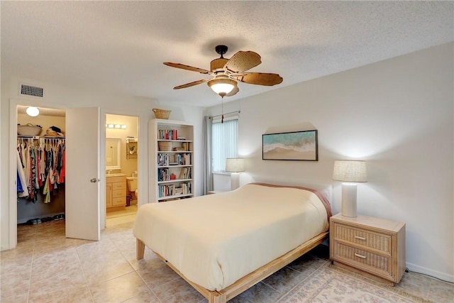 bedroom featuring a textured ceiling, a spacious closet, ceiling fan, a closet, and ensuite bath