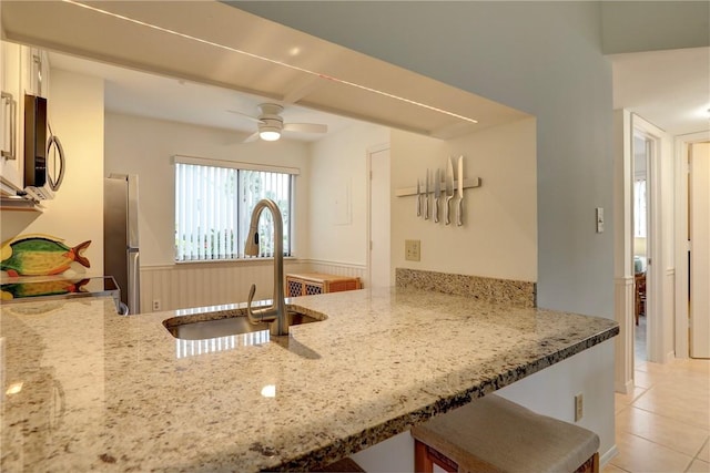 kitchen featuring light stone countertops, stainless steel appliances, light tile patterned floors, ceiling fan, and sink