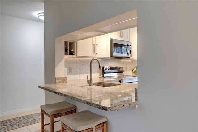 kitchen with stainless steel appliances, sink, kitchen peninsula, light stone countertops, and a breakfast bar