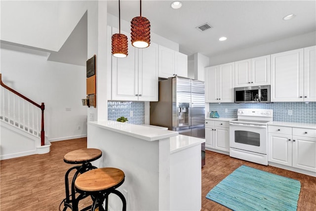 kitchen with a breakfast bar, white cabinetry, decorative light fixtures, stainless steel appliances, and kitchen peninsula