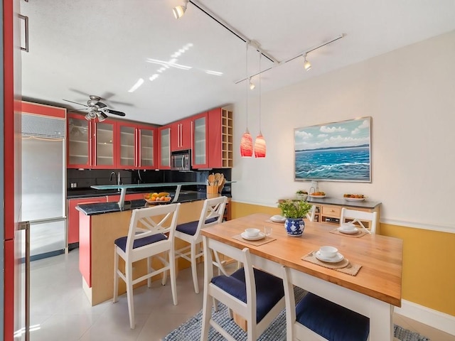 kitchen with track lighting, glass insert cabinets, dark countertops, a breakfast bar area, and stainless steel appliances