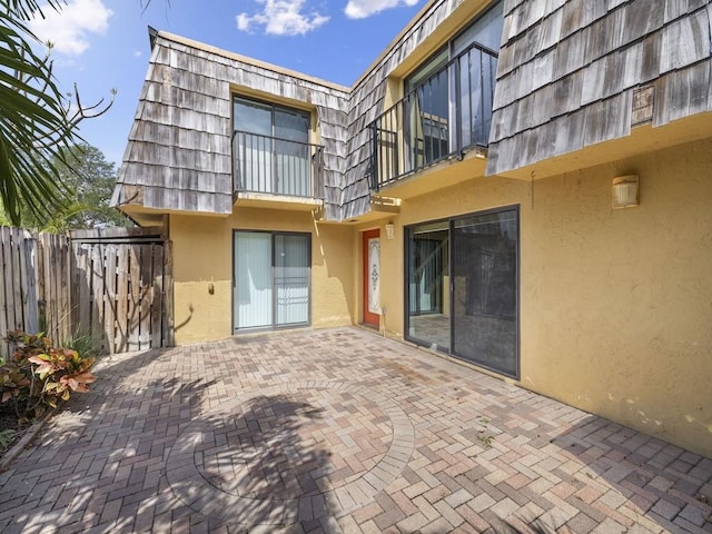 rear view of property featuring mansard roof, a patio area, stucco siding, and fence