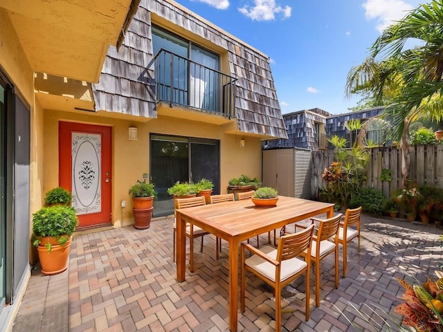 view of patio / terrace featuring a storage shed, outdoor dining space, fence, an outdoor structure, and a balcony