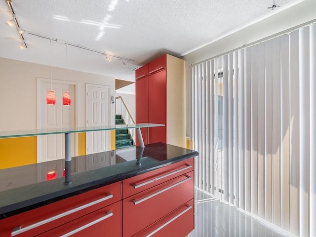 kitchen with track lighting, dark countertops, red cabinetry, and a textured ceiling