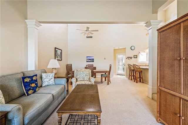 carpeted living room with ceiling fan, decorative columns, and a high ceiling