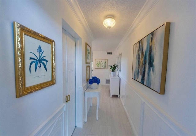 hallway with crown molding, a decorative wall, visible vents, and a textured ceiling