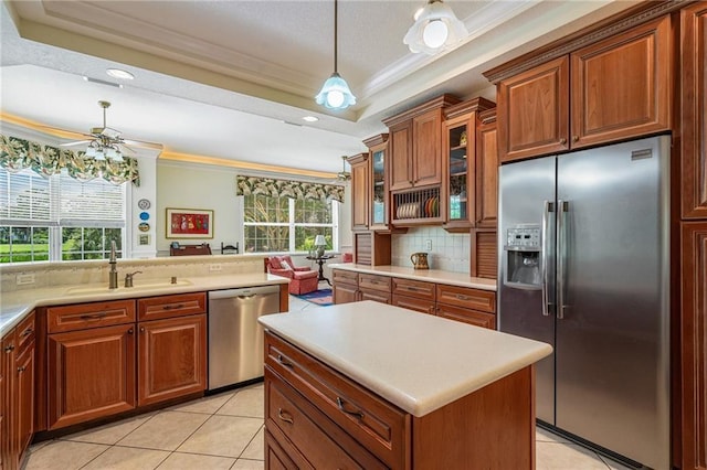 kitchen featuring stainless steel appliances, a raised ceiling, light countertops, glass insert cabinets, and a sink