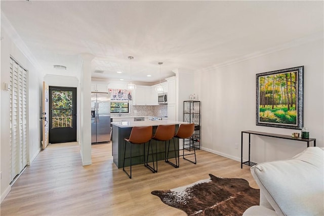 kitchen featuring a breakfast bar, stainless steel appliances, light countertops, white cabinets, and crown molding