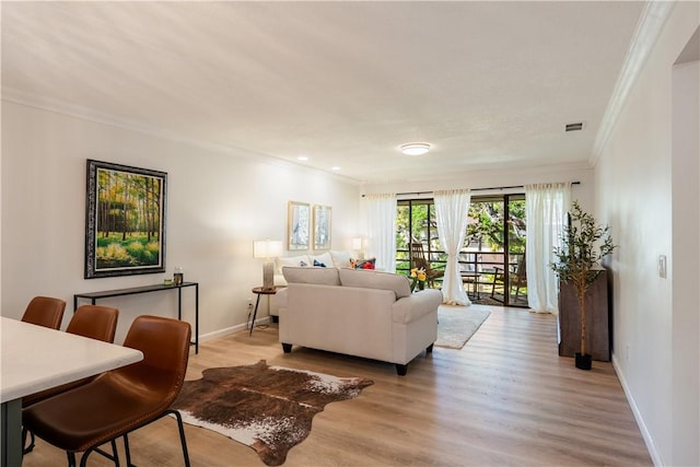 living area featuring visible vents, baseboards, light wood-style floors, and ornamental molding