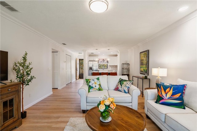 living room with baseboards, visible vents, light wood finished floors, and ornamental molding