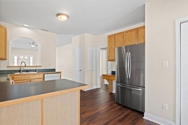 kitchen featuring dark countertops, dark wood finished floors, freestanding refrigerator, white dishwasher, and a sink