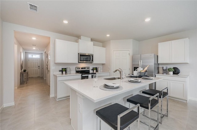 kitchen featuring visible vents, an island with sink, a sink, appliances with stainless steel finishes, and a breakfast bar area