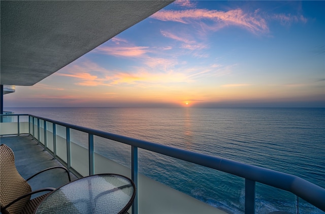 balcony at dusk featuring a water view