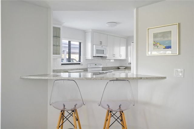 kitchen with a breakfast bar area, white cabinetry, kitchen peninsula, white appliances, and backsplash